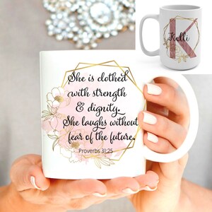 Könnte beinhalten: Weiße Keramiktasse mit goldenem geometrischem Design und rosafarbenen Aquarell-Blumenakzenten. Die Tasse trägt den Text "She is clothed with strength & dignity. She laughs without fear of the future. Proverbs 31:25".