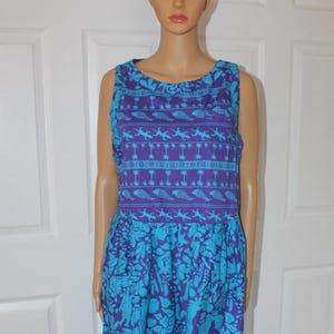 Könnte beinhalten: Ein ärmelloses, bodenlanges Kleid in Blau- und Lilatönen. Das Oberteil hat ein sich wiederholendes Muster aus Fischen und Palmen, während der Rock ein florales Design hat. Das Kleid wird auf einer Schaufensterpuppe präsentiert.