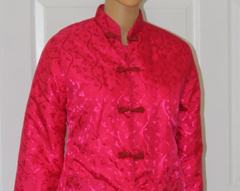 Puede incluir: Una chaqueta acolchada rosa con un estampado floral y cierres de botón marrón. La chaqueta tiene un cuello mandarín y mangas largas.