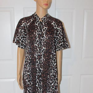 May include: A floor-length house dress featuring a brown, black, and white leopard print pattern. The garment has short sleeves, a collared neckline, and a button-down front closure that extends from the collar down to the mid-section of the dress.