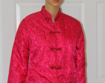 Puede incluir: Una chaqueta acolchada rosa con cuello mandarín y estampado floral. La chaqueta tiene cinco botones rojos con cierres anudados.