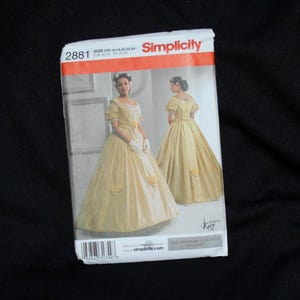 May include: A Simplicity sewing pattern envelope 2881 for a floor-length yellow gown with puff sleeves and a full skirt. The front shows the dress from two angles, with text including size U5 16, 18, 20, 22, 24 and The Museum Curator by Kay.