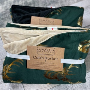 Photo with 2 variations of the Majestic Stag Cabin Blanket. Hunter Green Blanket with Gold Majestic Stags. Vintage Deer print throw blankets from The Kawartha sign & Pillow Co. Options for tan or black backing.