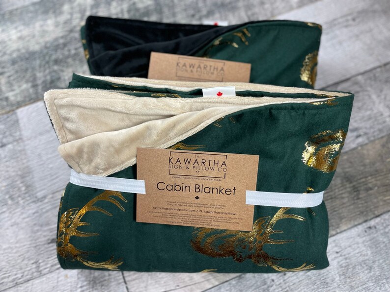 Photo with 2 variations of the Majestic Stag Cabin Blanket. Hunter Green Blanket with Gold Majestic Stags. Vintage Deer print throw blankets from The Kawartha sign & Pillow Co. Options for tan or black backing.