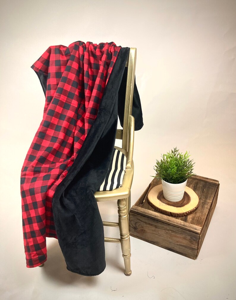 May include: A red and black buffalo plaid throw blanket with a black fleece backing. The blanket is draped over a wooden chair with a black and white striped cushion.