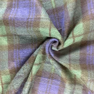 May include: A close-up of a soft, fuzzy fabric with a green, brown, and purple plaid pattern. The fabric is folded and twisted, showing the texture and colour variations.