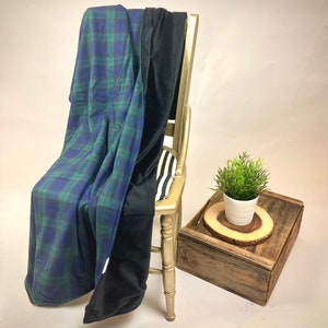 May include: A blue and green plaid blanket draped over a gold chair, with a black blanket folded over it. A small plant in a white pot sits on a wooden tray.