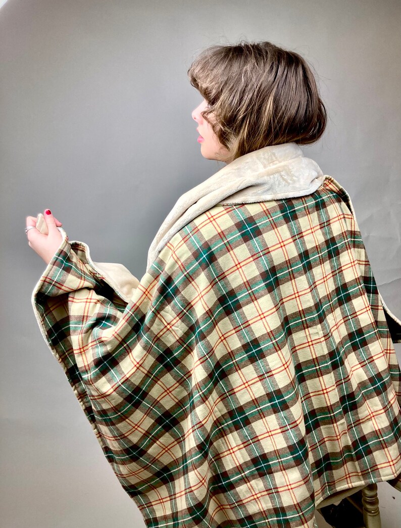 May include: A plaid throw blanket with a cream, brown, and green plaid pattern. The blanket has a soft, plush lining.