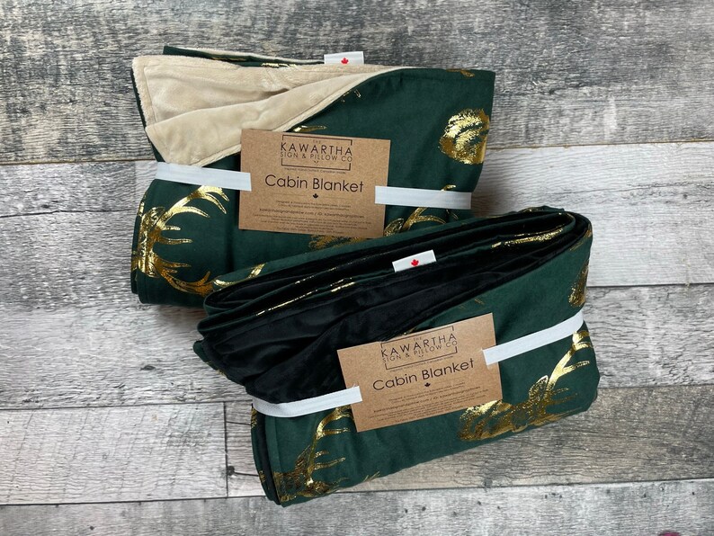 Photo with 2 throw blankets from The Kawartha Sign & Pillow Co, Hunter green throw with a gold foil stag print, backing options in black and tan chenille