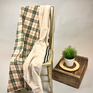 May include: A plaid and cream-colored throw blanket draped over a wooden chair. The blanket has a soft, plush texture and is perfect for cuddling up on the couch.