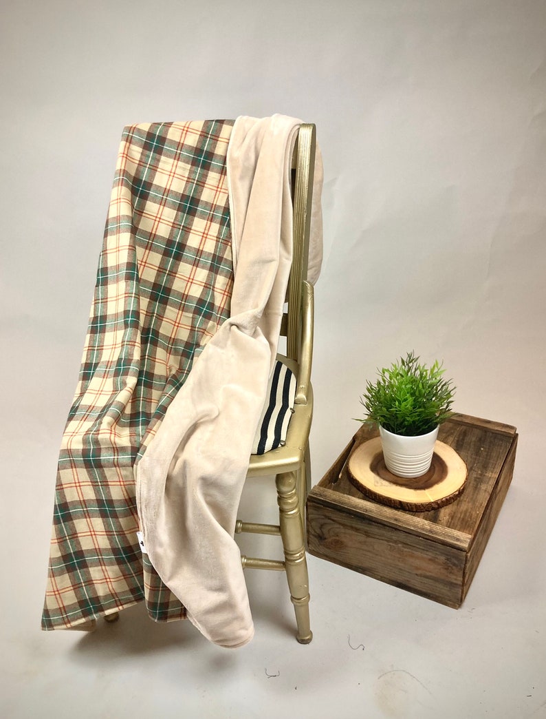 May include: A plaid and cream-colored throw blanket draped over a wooden chair. The blanket has a soft, plush texture and is perfect for cuddling up on the couch.