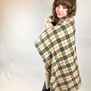 May include: A person wearing black jeans and a plaid blanket with brown, green, and white squares. The blanket is folded over the person's shoulders and is being held in their arms.