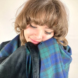 May include: A cozy blanket with a blue, green, and black plaid pattern. The blanket has a soft, dark gray, plush backing. The blanket is wrapped around a person.