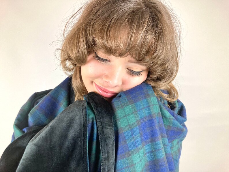 May include: A cozy blanket with a blue, green, and black plaid pattern. The blanket has a soft, dark gray, plush backing. The blanket is wrapped around a person.