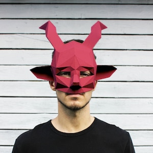 May include: A person wearing a red paper mask with horns and a black long-sleeved shirt. The mask is geometric and has a sharp, angular design.