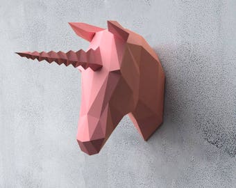 May include: A pink papercraft unicorn head mounted on a gray wall. The unicorn has a long, spiraled horn.