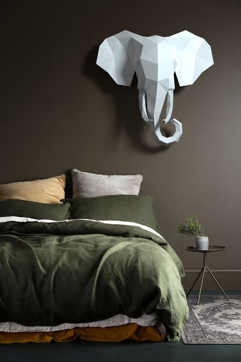 May include: A green linen duvet cover with a white stripe and a mustard yellow sheet underneath. The bed is styled with two pillows, one mustard yellow and one gray. A white origami elephant head is hanging on the wall above the bed.
