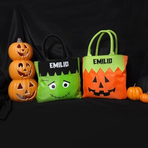 May include: Two green and orange Halloween trick or treat bags with the name "Emili" printed on them. One bag features a Frankenstein monster design and the other a jack-o-lantern design.