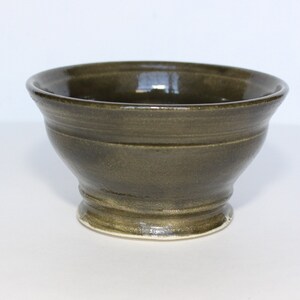 May include: A small, dark green ceramic bowl with a rounded base and a slightly flared rim. The bowl has a smooth, glossy finish.