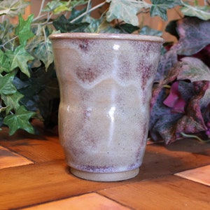 May include: A ceramic mug with a light brown glaze and a speckled purple and white design.