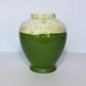 May include: A green ceramic vase with a white top and yellow speckles. The vase has a rounded body and a flared base.