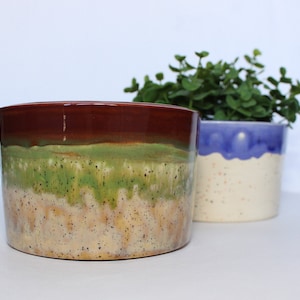 May include: Two ceramic planters, one with a brown, green, and beige glaze and the other with a blue and white glaze. Both planters have a speckled finish.