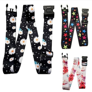 May include: Three luggage straps with different patterns. The first strap has a black background with white daisies. The second strap has a black background with colourful stars. The third strap has a white background with red and pink flowers. Each strap has a combination lock.