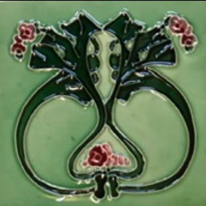 May include: A green ceramic tile featuring a black and white floral design. The flowers are stylised and have pink centres. The tile has a glossy finish.
