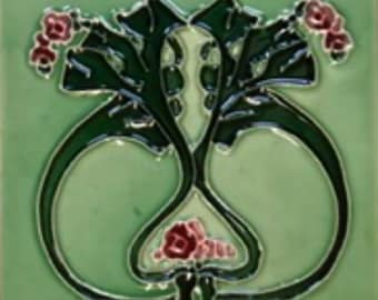 May include: A green ceramic tile with a black and white floral design. The flowers are stylized and have pink centers. The tile has a glossy finish.