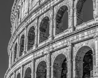 May include: A black and white photo of the Colosseum in Rome, Italy. The photo shows the exterior of the building, with its many arches and columns.