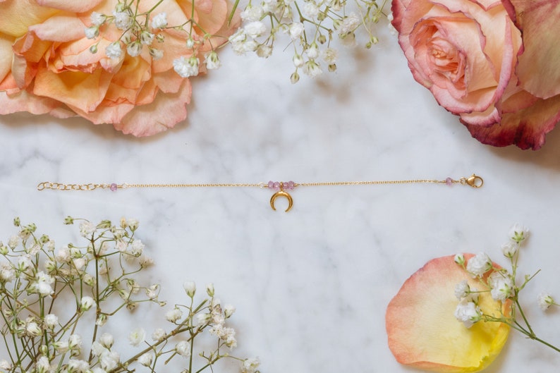 Puede incluir: Un delicado brazalete de cadena dorada con un dije de luna creciente y peque&ntilde;as cuentas moradas.