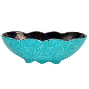 May include: A turquoise ceramic bowl with a black rim and a speckled glaze. The bowl has a wavy edge and a rounded base.