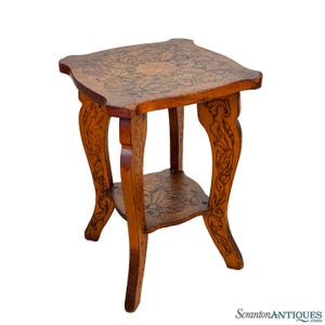 May include: A small, intricately carved wooden table with a square top and a lower shelf. The table has a floral design carved into the wood, and the legs are curved and ornate.