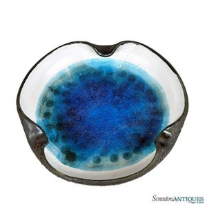 May include: A round ceramic bowl featuring a deep blue center with a visible crackle glaze finish, transitioning into a lighter turquoise gradient. The wide, smooth white rim is framed by a dark, textured, charcoal-colored outer edge.