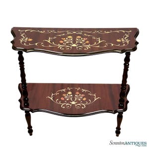 May include: A two-tiered, dark wood side table with floral inlay. The table has a curved top and bottom shelf, supported by turned legs. The floral design includes cream, orange, and yellow accents. The table is approximately 30 inches long.