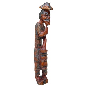 May include: A wooden carving of a person wearing a hat and traditional clothing. The carving is painted in shades of brown, black, and red.