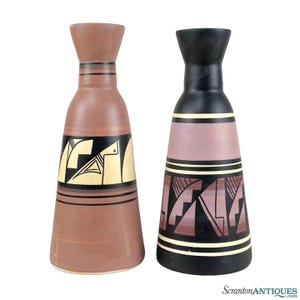 May include: Two ceramic vases with geometric designs. The vase on the left is brown with yellow and black accents. The vase on the right is black with pink, yellow, and black accents.