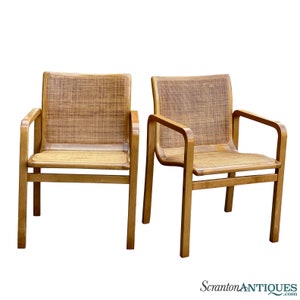 May include: Two wooden chairs with woven cane seats and backs. The chairs have a simple, mid-century modern design.