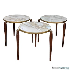 May include: Set of three round nesting tables with white marble tops and gold trim. The tables have dark wood legs.