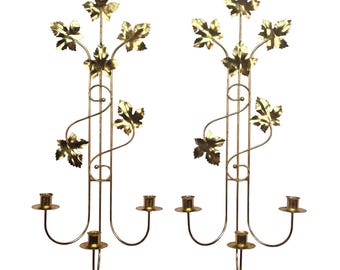 May include: A pair of gold metal wall sconces with a vine and leaf design. Each sconce has three candle holders.