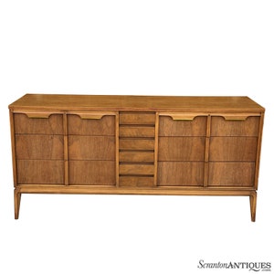 May include: A mid-century modern dresser with six drawers and brass hardware. The dresser is made of wood and has a light brown finish.