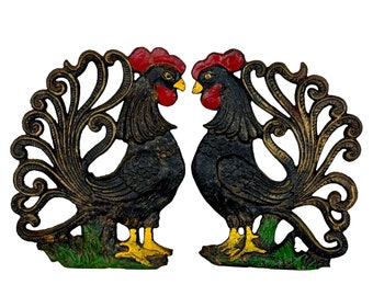 May include: A pair of black cast iron rooster figurines with red and gold accents. The roosters are facing each other with their tails spread out in a decorative design.