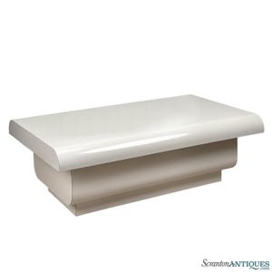 May include: A rectangular, off-white coffee table with a glossy finish. The table has rounded edges and a solid base. The design is modern and minimalist, suitable for a living room or lounge area.
