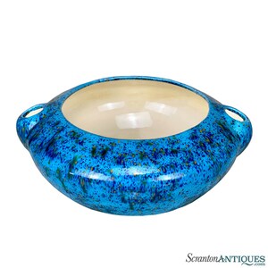 May include: A large, blue ceramic serving bowl with two handles. The bowl has a speckled glaze with gold flecks. The inside of the bowl is white.