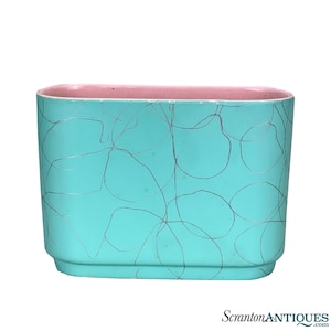 May include: A turquoise planter with a pink rim and a silver swirl design. The planter is oval shaped and has a smooth, glossy finish.