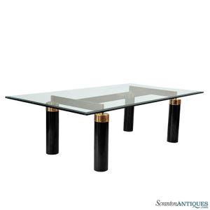 May include: Rectangular glass-top coffee table with black cylindrical legs and gold-toned metal accents. The table's dimensions are approximately 60 inches long and 30 inches wide, with a height of 16 inches.