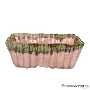 May include: A rectangular pink planter with a green and brown glaze. The planter has a scalloped edge and a design of vertical lines.