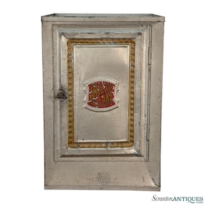 May include: Vintage metal bread and cake cabinet with a silver finish. The cabinet features a rectangular design with a door, a decorative gold border, and the words "Bread & Cake Cabinet" in red lettering.