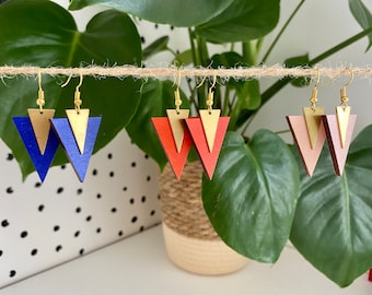 Könnte beinhalten: Drei Paare geometrische Dreiecksohrringe mit goldenen Akzenten. Die Ohrringe sind aus Holz und in Blau, Rot und Rosa erhältlich.