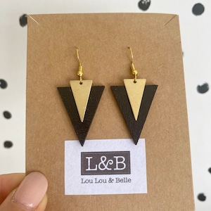 May include: A pair of black and gold triangle earrings with gold hooks. The earrings are displayed on a brown card with the text "L&B Lou Lou & Belle".